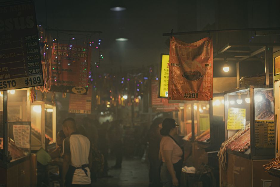 Explore a atmosfera movimentada de um mercado noturno em Oaxaca, México, com letreiros vibrantes e vendedores locais.